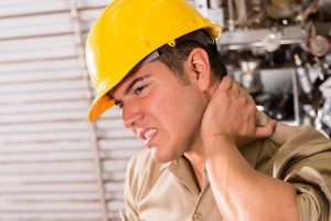 Man wearing hardhat feeling the back of his neck in pain as he awaits a medical examination